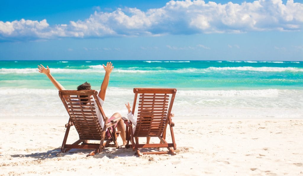 Young father with little daughter in beach chairs raised their hands up on white sand beach