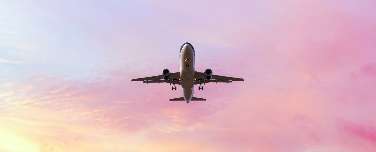 Landing airplane on the pastel colored sky background. Sunset sky in the pink and blue colors "n