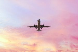 Landing airplane on the pastel colored sky background. Sunset sky in the pink and blue colors "n