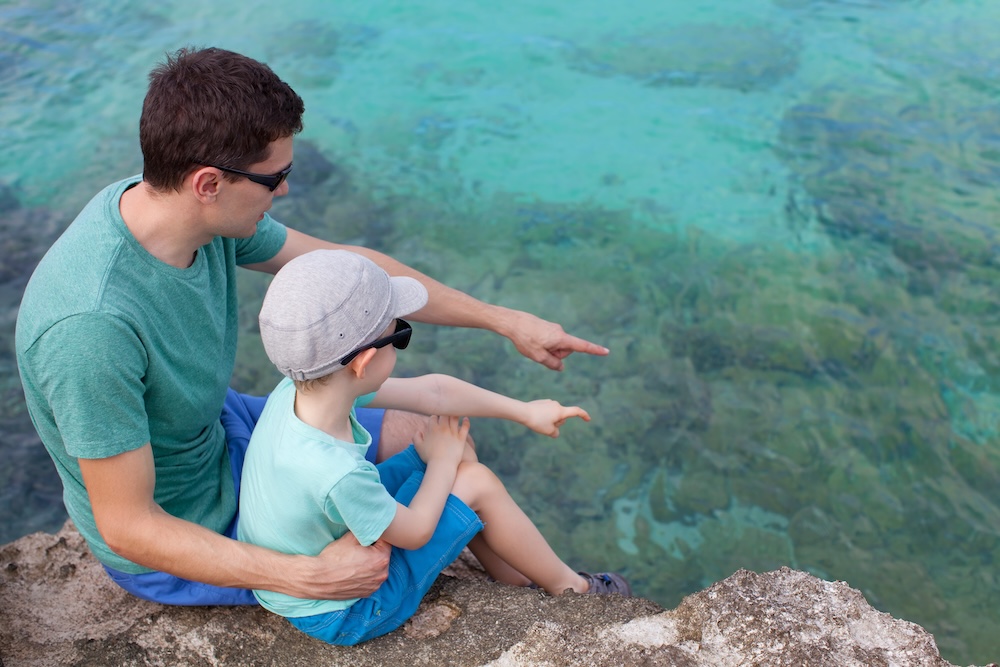 Young father and his son sitting at the rocky beach and exploring underwater life.