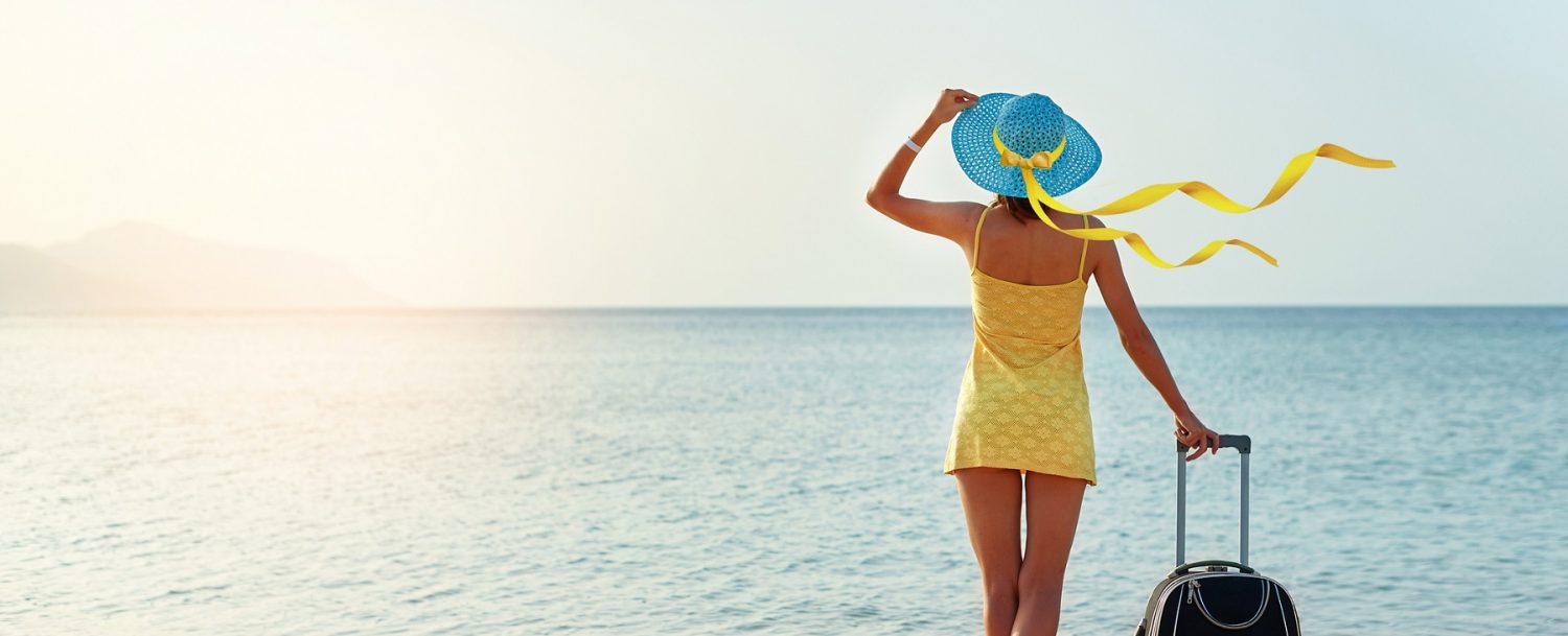 Beautiful young woman with a hat standing with suitcase on the wonderful sea background, concept of time to travel, with space for your text