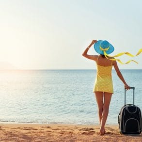 Beautiful young woman with a hat standing with suitcase on the wonderful sea background, concept of time to travel, with space for your text