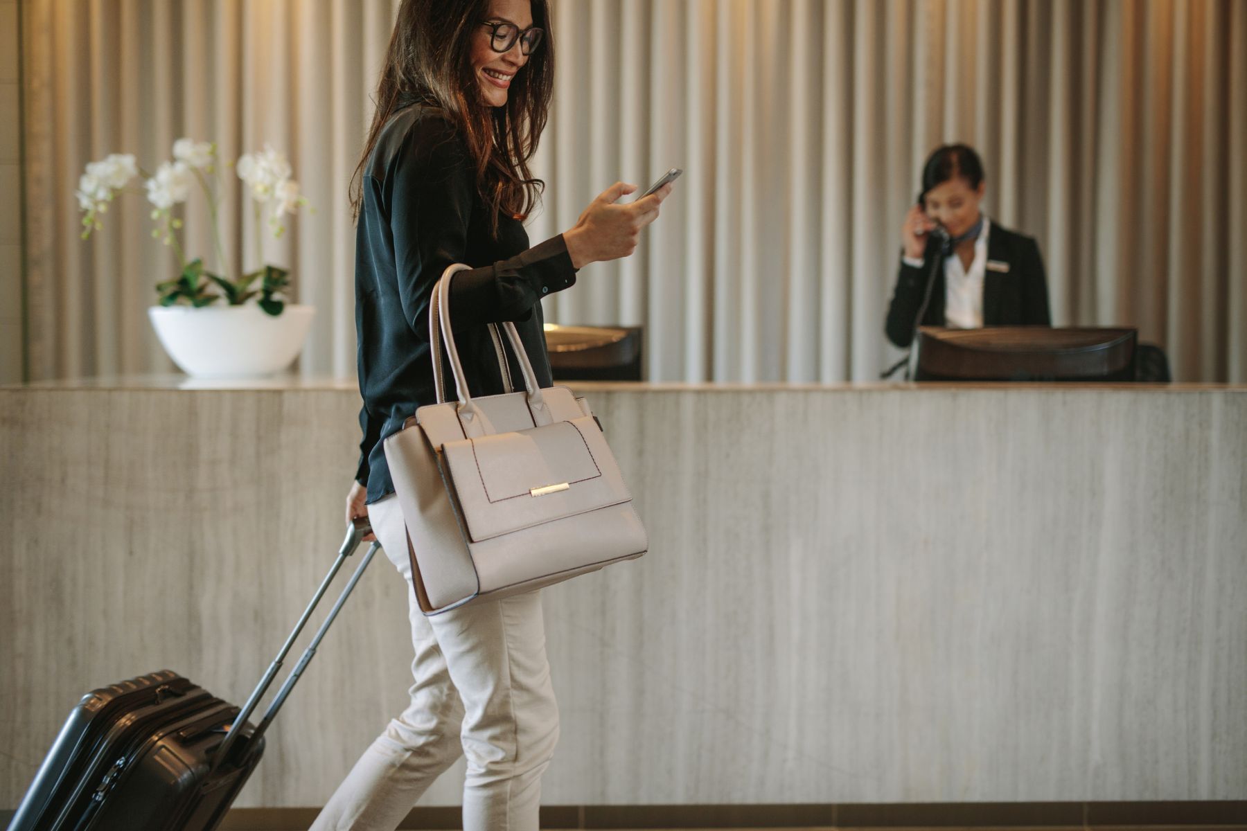woman with her luggage and bag walking through a lobby
