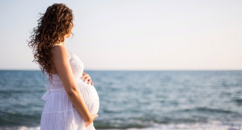 Young pregnant woman walking on the beach.